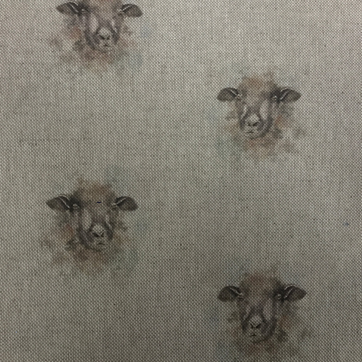 A close-up of a woven fabric with a repeating pattern of sheep faces in muted brown and gray tones on a light beige background.