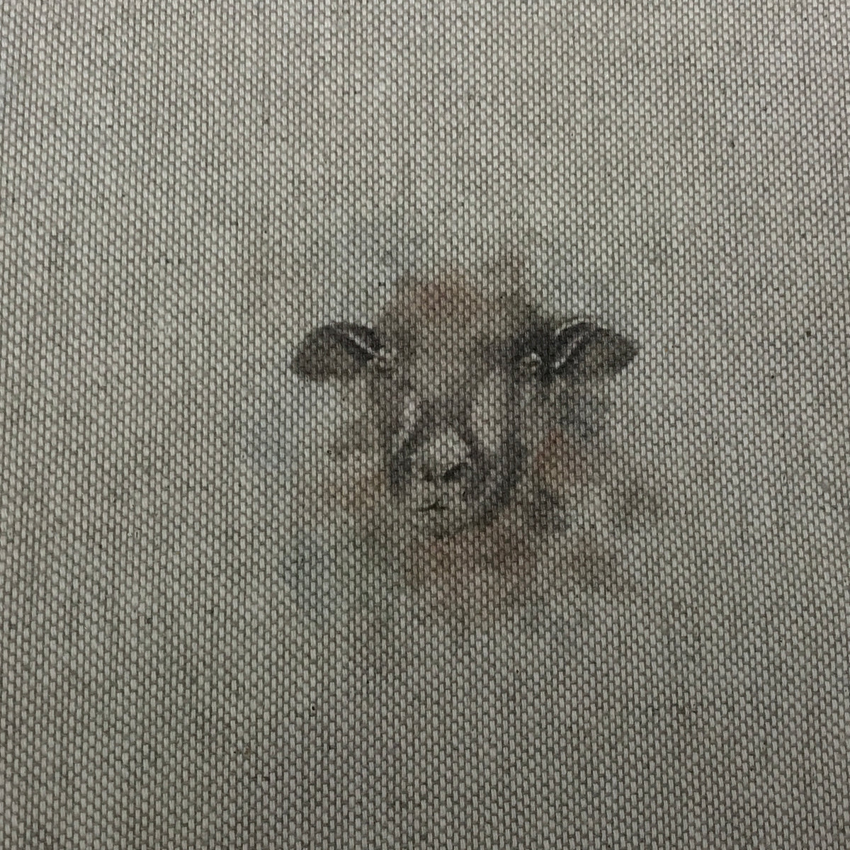 A close-up of woven fabric with a small embroidered or printed sheep face motif in muted brown and gray tones at the center.