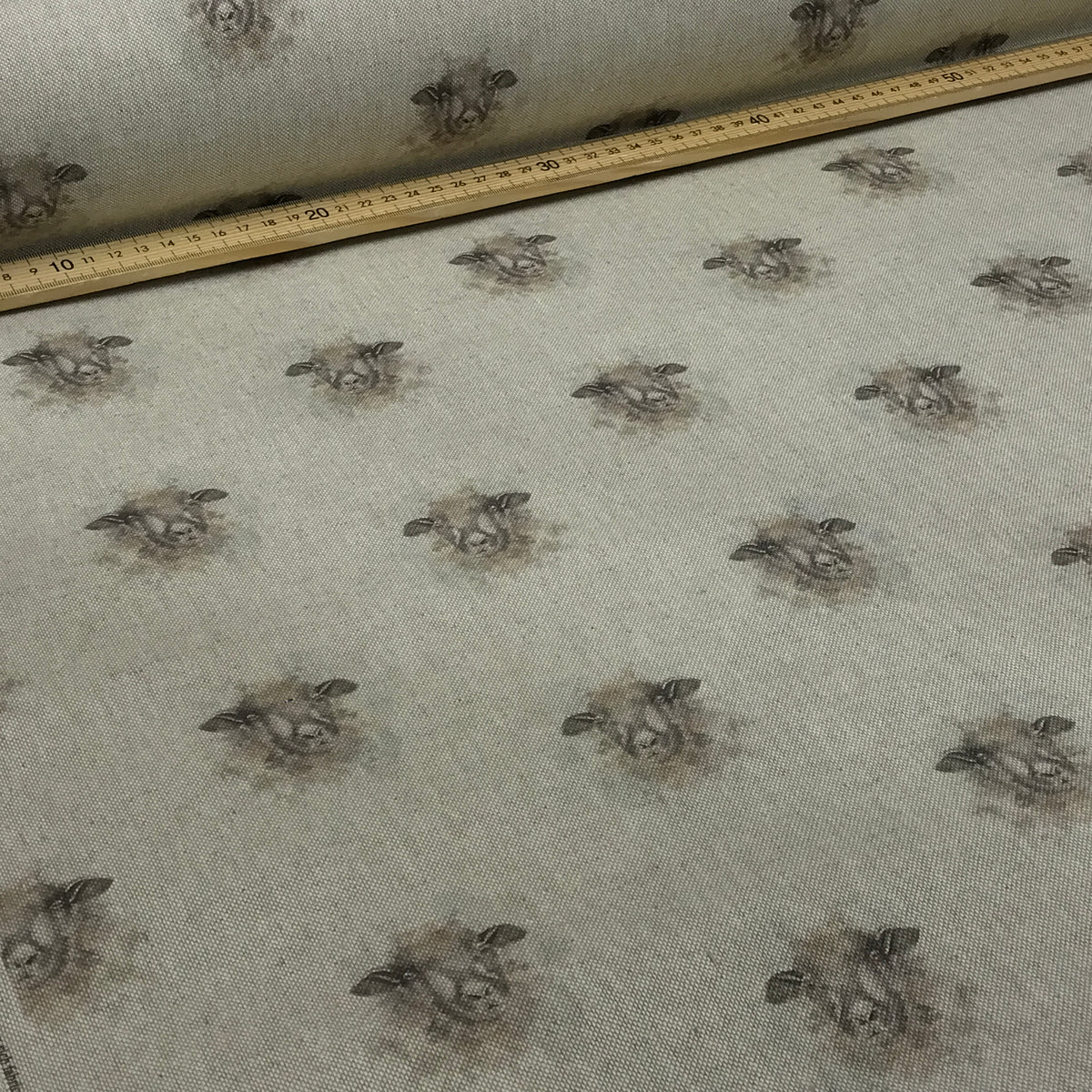 A close-up of patterned fabric with a repeating cow print on a light beige background, with a wooden ruler placed along the top edge for scale.