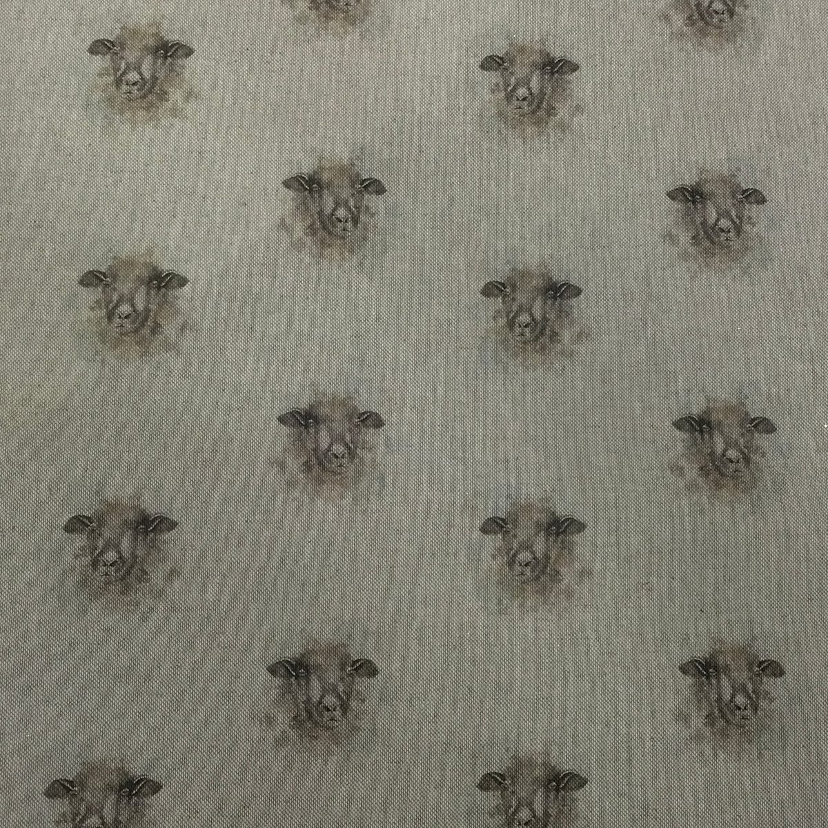 A close-up of fabric featuring a repeating pattern of sheep heads in muted brown and gray tones on a light warm gray background.
