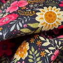 A close-up of a floral fabric with a black background, featuring large yellow sunflowers, red and pink flowers, and green leaves.