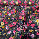 A close-up of a dark floral fabric with a dense pattern of pink, red, yellow, and white flowers with green leaves on a black background.