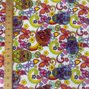 A close-up of a white fabric with a colorful retro sugar skull and peace sign pattern, shown next to a wooden ruler for scale.