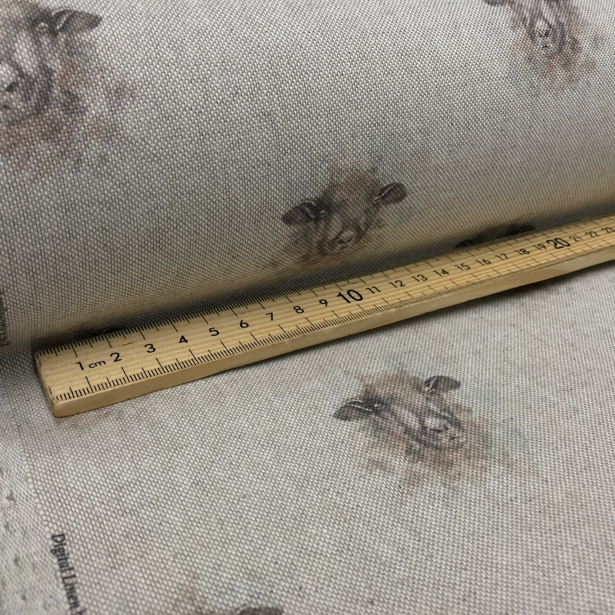 A close-up of a roll of fabric with a sheep print, placed next to a wooden ruler to show the scale of the pattern.