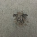 A close-up of woven fabric with a small embroidered or printed sheep face motif in muted brown and gray tones at the center.