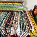 A large collection of folded and stacked patterned fabrics in various colors and designs, including floral, animal, and abstract prints, arranged on shelves.