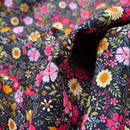 A close-up of a folded piece of fabric with a dense floral print on a black background, featuring pink, yellow, white, and green flowers and leaves.