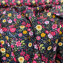 A close-up of draped fabric with a dense floral print on a dark navy background, featuring pink, red, yellow, and white flowers with green leaves.
