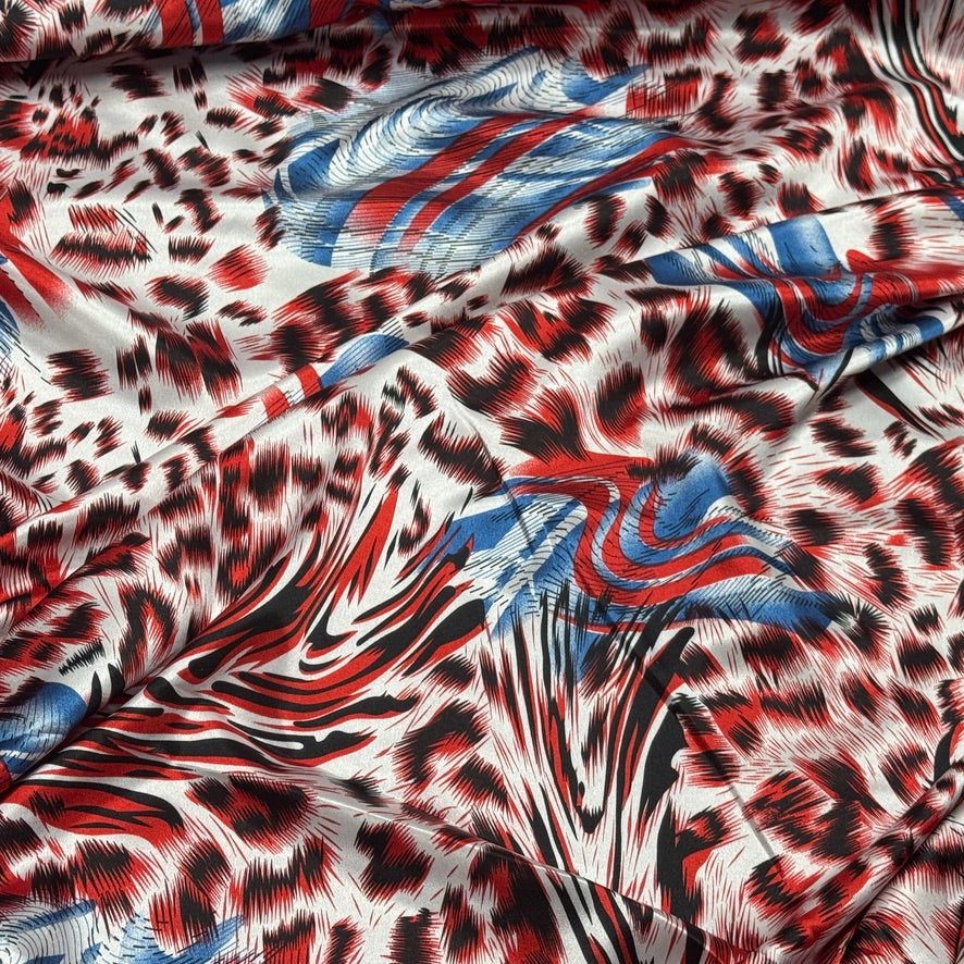 A close-up of draped fabric featuring an abstract print with a leopard-like black and red pattern over a white base, overlaid with blue and red brushstroke and feather-like motifs.