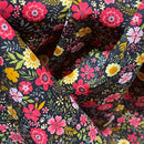 A close-up of draped fabric featuring a dense floral pattern with pink, red, yellow, and white flowers on a dark charcoal background.