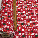 Red floral fabric with a repeating pattern of white, green, and small orange flowers, shown partially rolled with a wooden ruler for scale.