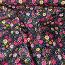 A close-up of a draped fabric with a dense, all-over floral print on a dark navy background. The pattern features pink, red, yellow, and white flowers with green leaves.