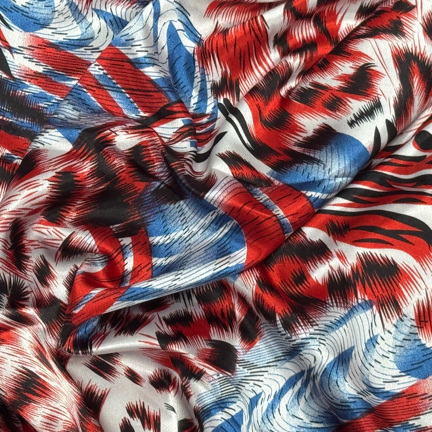 A close-up of draped fabric with an abstract print in red, blue, black, and white, featuring blended brushstroke and flag-inspired patterns.