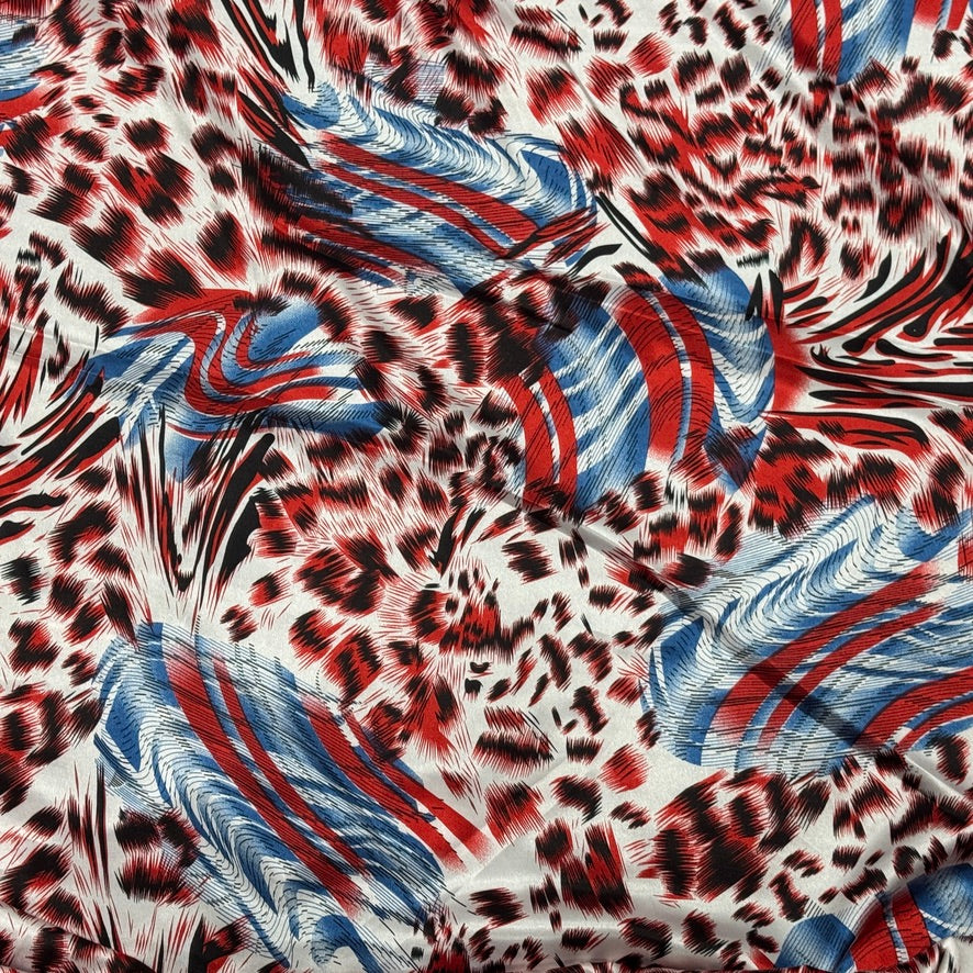 A close-up of a patterned fabric featuring a red, black, and white leopard print blended with blue and red feather-like motifs on a white base.