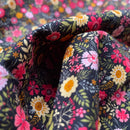 A close-up of draped fabric with a dense floral print on a dark background. The pattern features pink, yellow, white, and orange flowers with green leaves and stems.
