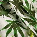 A close-up of a white fabric with a green cannabis leaf pattern, showing the woven texture and soft folds.