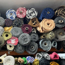 A dense collection of rolled knitted wool blends fabrics in a wide variety of colors and patterns, stacked tightly together on shelves.